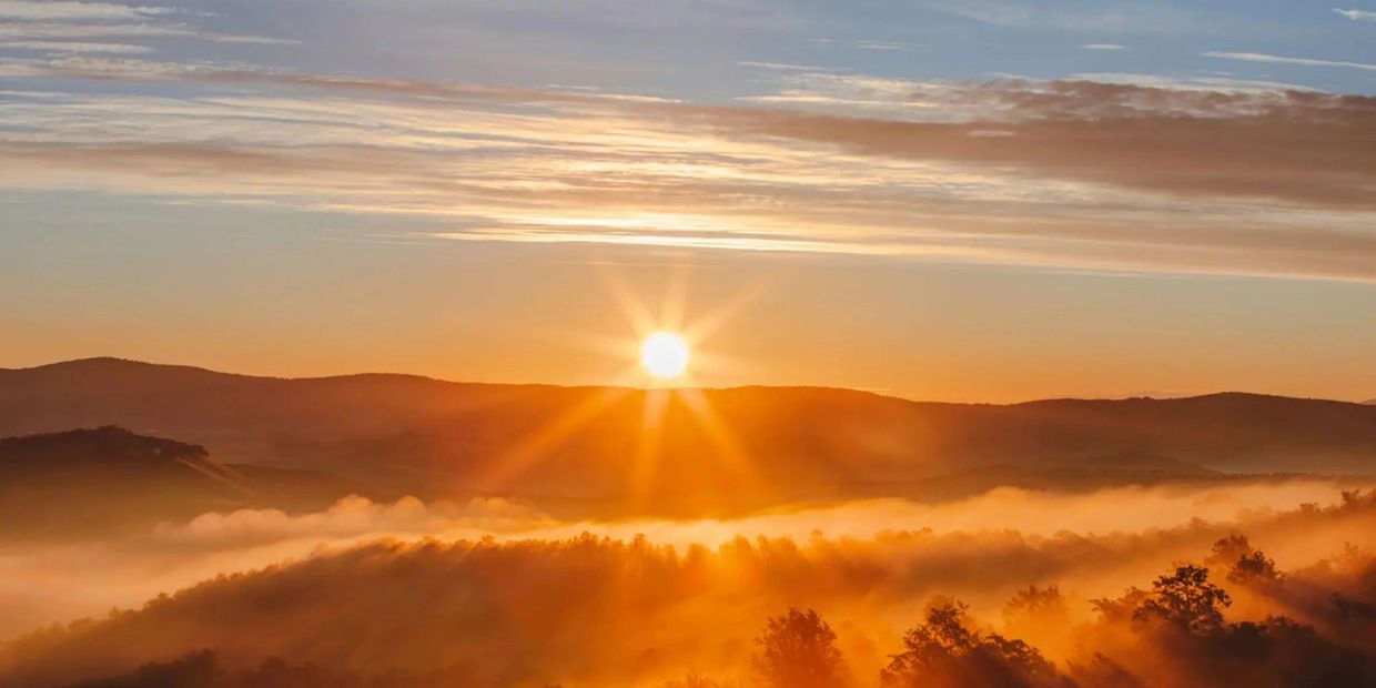 Sunrise casting golden rays over misty hills and trees.