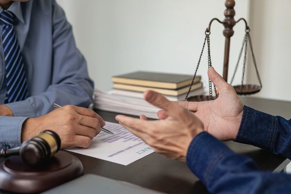 Two people discuss a legal contract with a gavel and scales of justice present.
