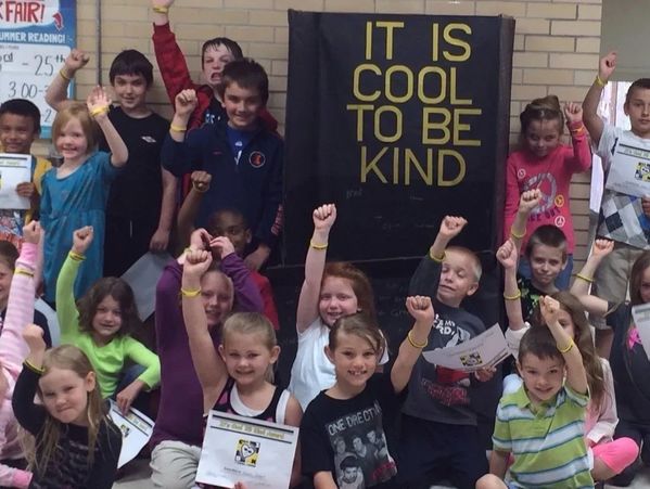 Group of children raising fists around a kindness poster.