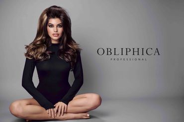 Model with voluminous hair and smoky eye makeup in black outfit, seated cross-legged.