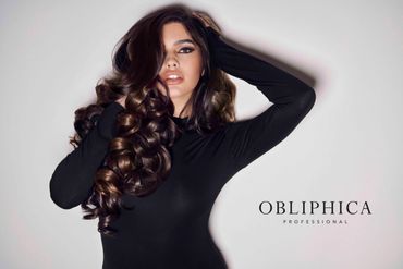 A woman with voluminous curly hair poses in black against a light background with Obliphica Professional branding.