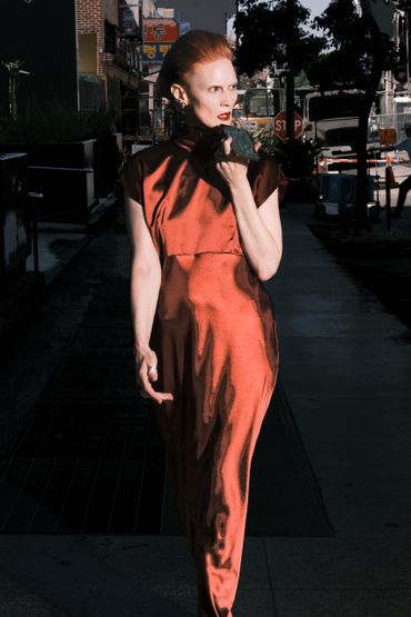 Woman in a shiny red dress walking on a city street, holding a phone.
