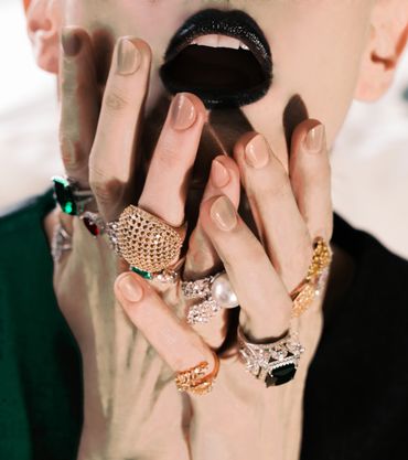 Close-up of hands with ornate rings and black lipstick on lips.