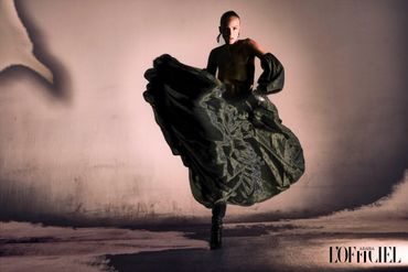 Model in flowing dark outfit striking a dynamic pose against a textured wall.