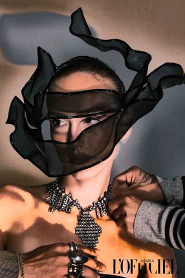 Fashion model with flowing black veil and sparkling necklace being styled.
