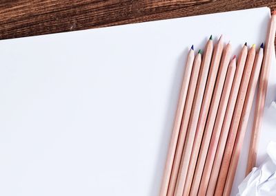Colored pencils on white paper with crumpled sheets nearby on wooden table.
