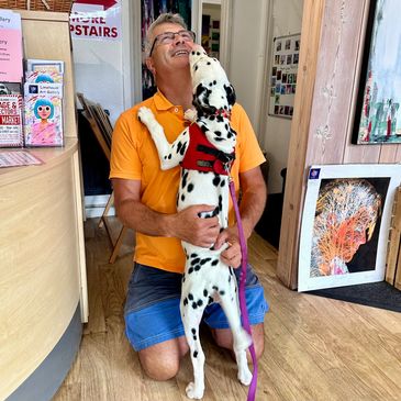 Man in orange shirt joyfully hugging a Dalmatian dog indoors.