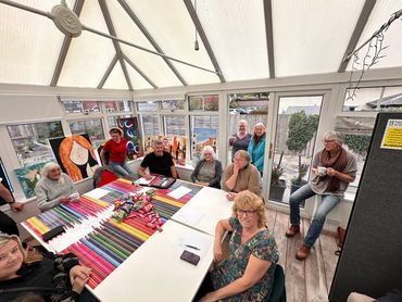 Group of people gathered around a table in a bright room with artwork and snacks.