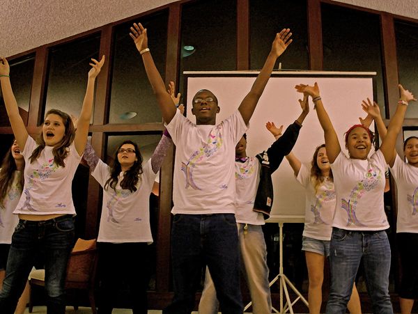 Group of young people raising their hands energetically indoors.