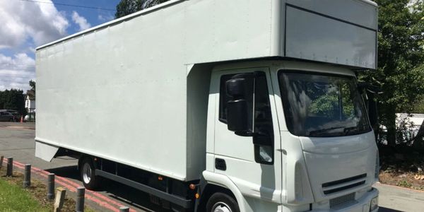 A large white box truck parked on a street under a partly cloudy sky.