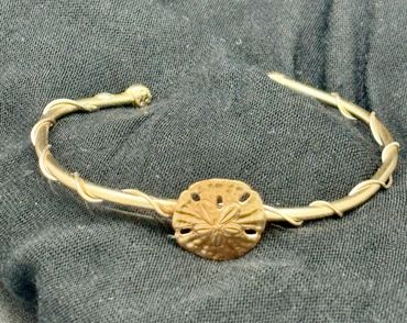 Gold bracelet with a sand dollar charm on black fabric.