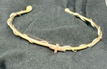 Gold bracelet with a cross design on black fabric.