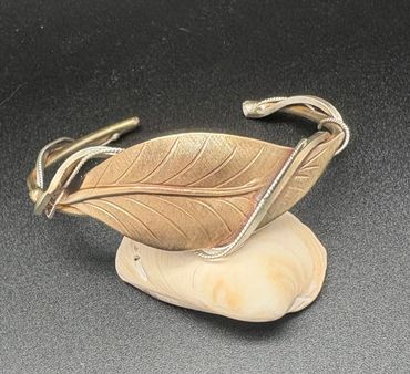 Intricately designed leaf-shaped bracelet on a seashell.