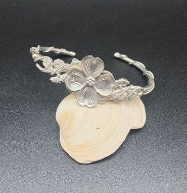 Silver floral bracelet with intricate leaf and vine details on a black background.