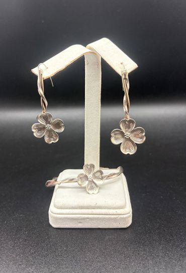 Silver floral earrings and matching bracelet set on a white stand.