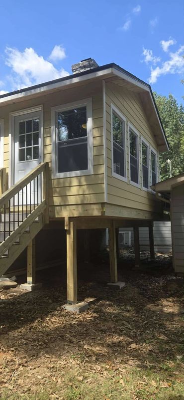 Yellow elevated house with white trim and multiple windows under a clear blue sky.