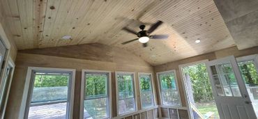 A cozy sunroom with wooden ceiling, multiple windows, and a ceiling fan.