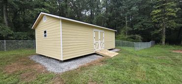 Yellow storage shed with a ramp in a grassy backyard near a chain-link fence.