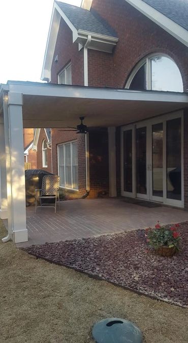 Covered patio with ceiling fan and brick house exterior.