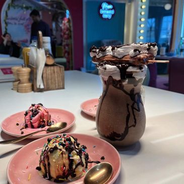 Decadent chocolate milkshake with ice cream scoops and sprinkles on pink plates.