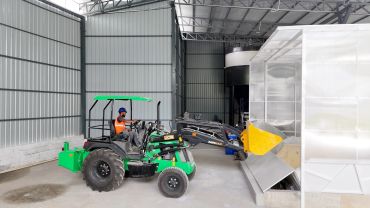 Worker operating green JCB loader inside a warehouse.