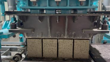 Industrial machine compressing cement blocks.