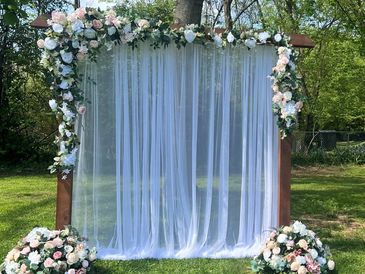 Elegant floral wedding arch with white drapes in a garden.
