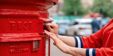 Person posting a letter into a red postbox outdoors.