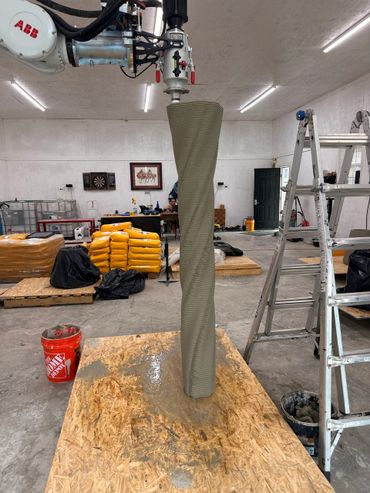 3D concrete printing in progress creating a tall, textured column indoors.