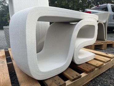 Modern white 3D-printed chairs with a smooth, curved design on wooden pallets outdoors.