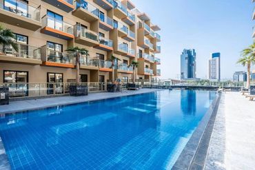 Modern apartment complex with a large outdoor swimming pool under clear blue sky.