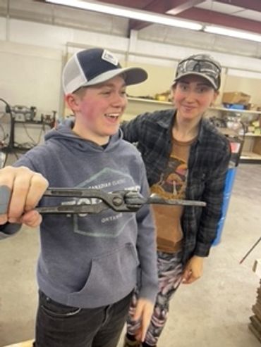Two students. One showing handiwork / craftsmanship holding a horse shoe.