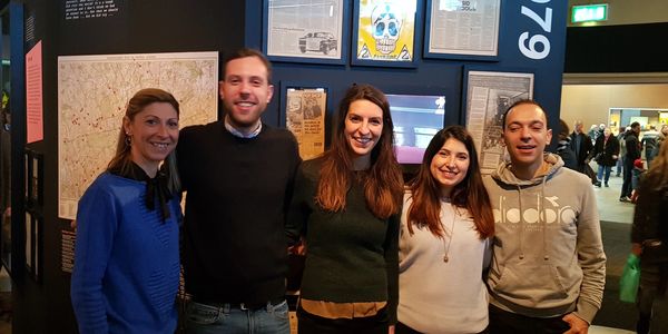 Group of five friends smiling indoors at an exhibition.