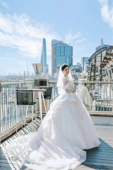 Bride in a white wedding dress smiling on a rooftop with city skyline background.