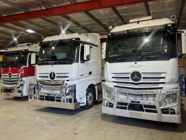 Three large white Mercedes-Benz trucks parked inside a warehouse.