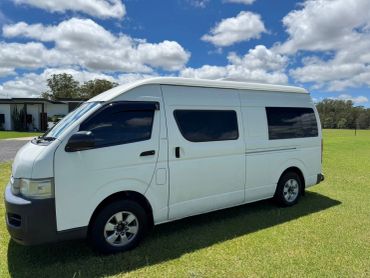 White van parked on grass under a blue sky with clouds.