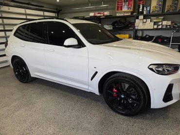 White BMW SUV with black wheels parked in a garage.