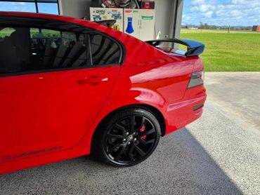 Red sports car with black rims parked in a garage with green field outside.
