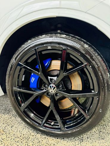 Close-up of a Volkswagen car wheel with black alloy rim and blue brake caliper.