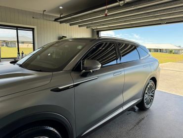 Sleek gray SUV parked inside a garage with a view of houses outside.
