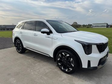 White modern SUV parked on concrete with green fields in the background.
