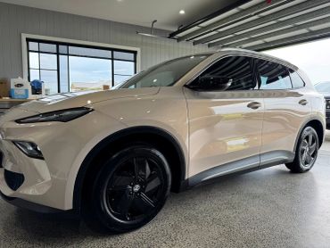 Beige SUV with black rims parked inside a garage with large windows.