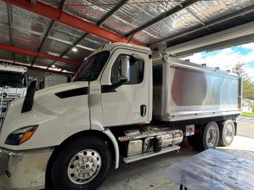 White heavy-duty truck inside a warehouse with a polished metal cargo bed.