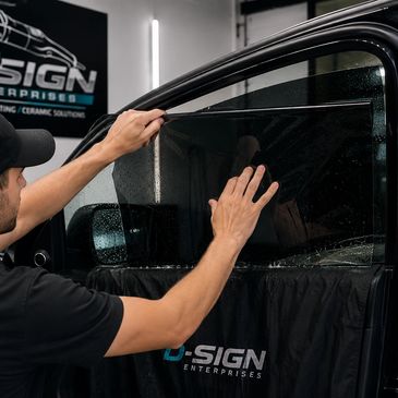 Technician applying window tint film on a car door at D-Sign Enterprises.