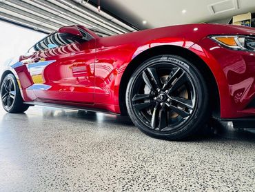 Shiny red sports car with black rims in a garage.