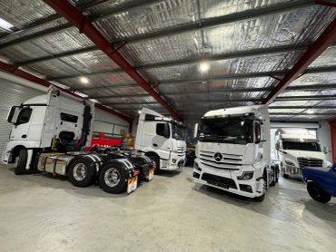 White Mercedes trucks parked inside a metal-roofed garage.