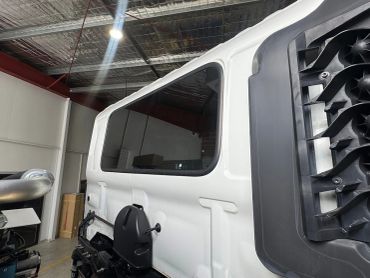 Close-up of a white truck cabin with a black side mirror and vent in a garage.