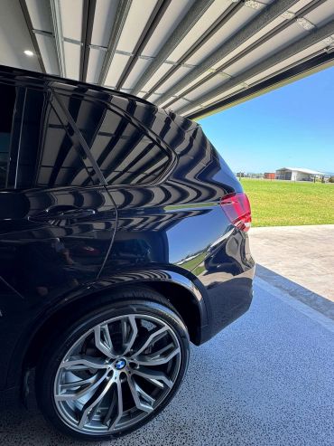 Close-up of a sleek black BMW car wheel and rear side under a garage roof.