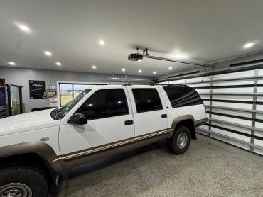 A white and brown SUV parked inside a clean garage with multiple ceiling lights.