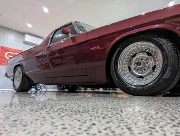 Low angle view of a shiny maroon classic car with polished chrome wheels indoors.